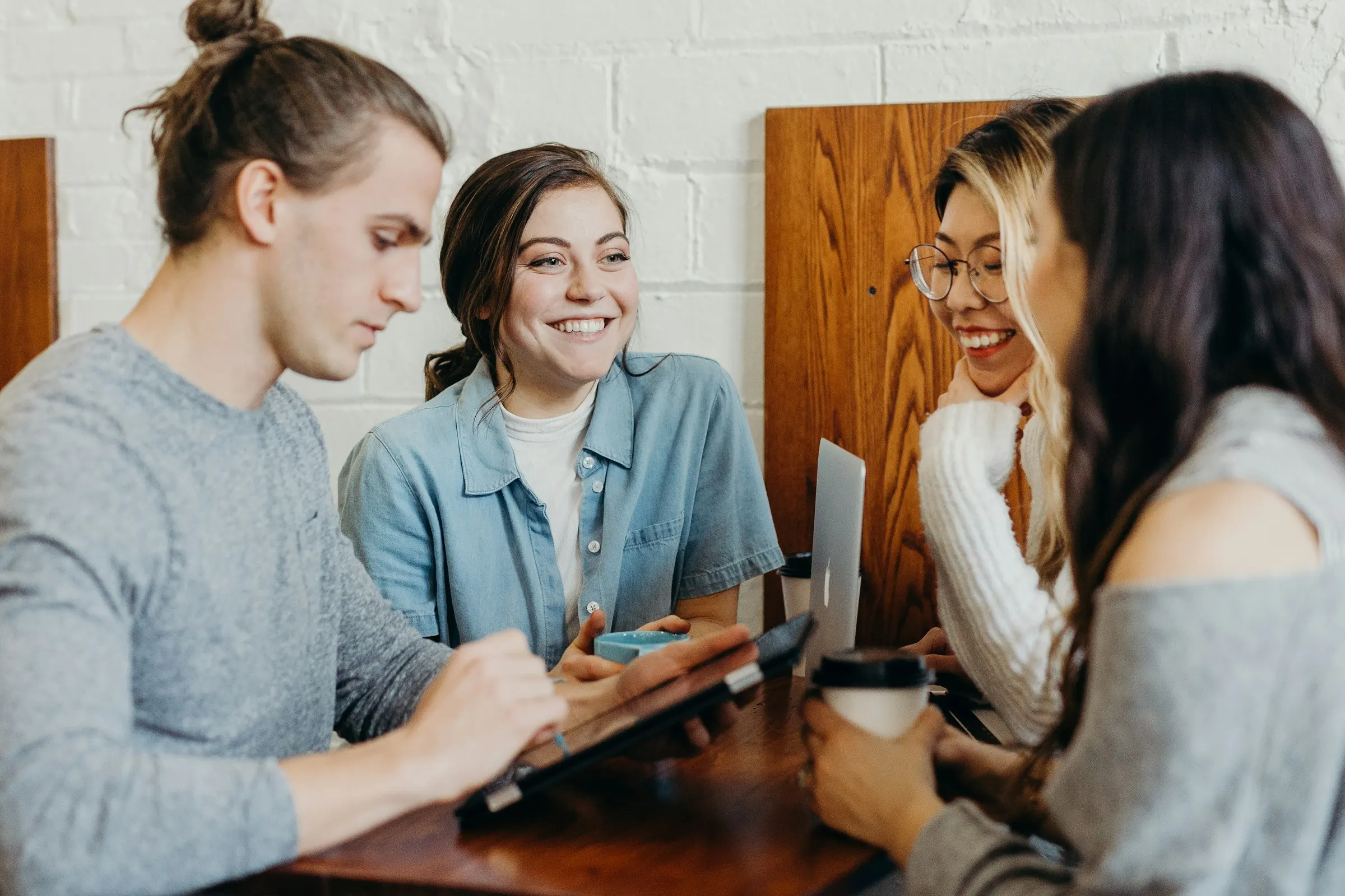 Quatro pessoas conversam em volta de uma mesa, com café e um tablet.